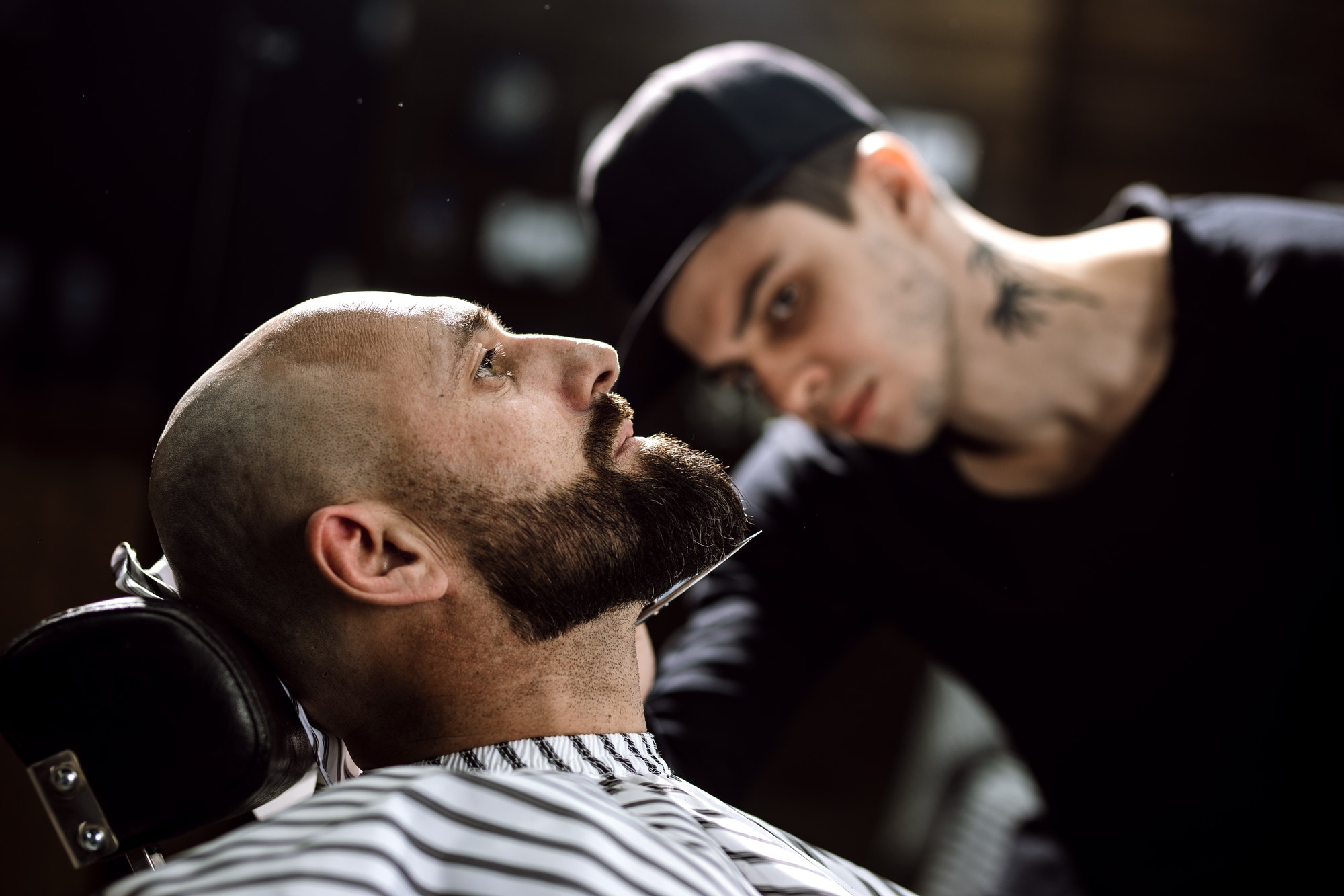 The barber dressed in a black clothes scissors beard of brutal man in the stylish barbershop